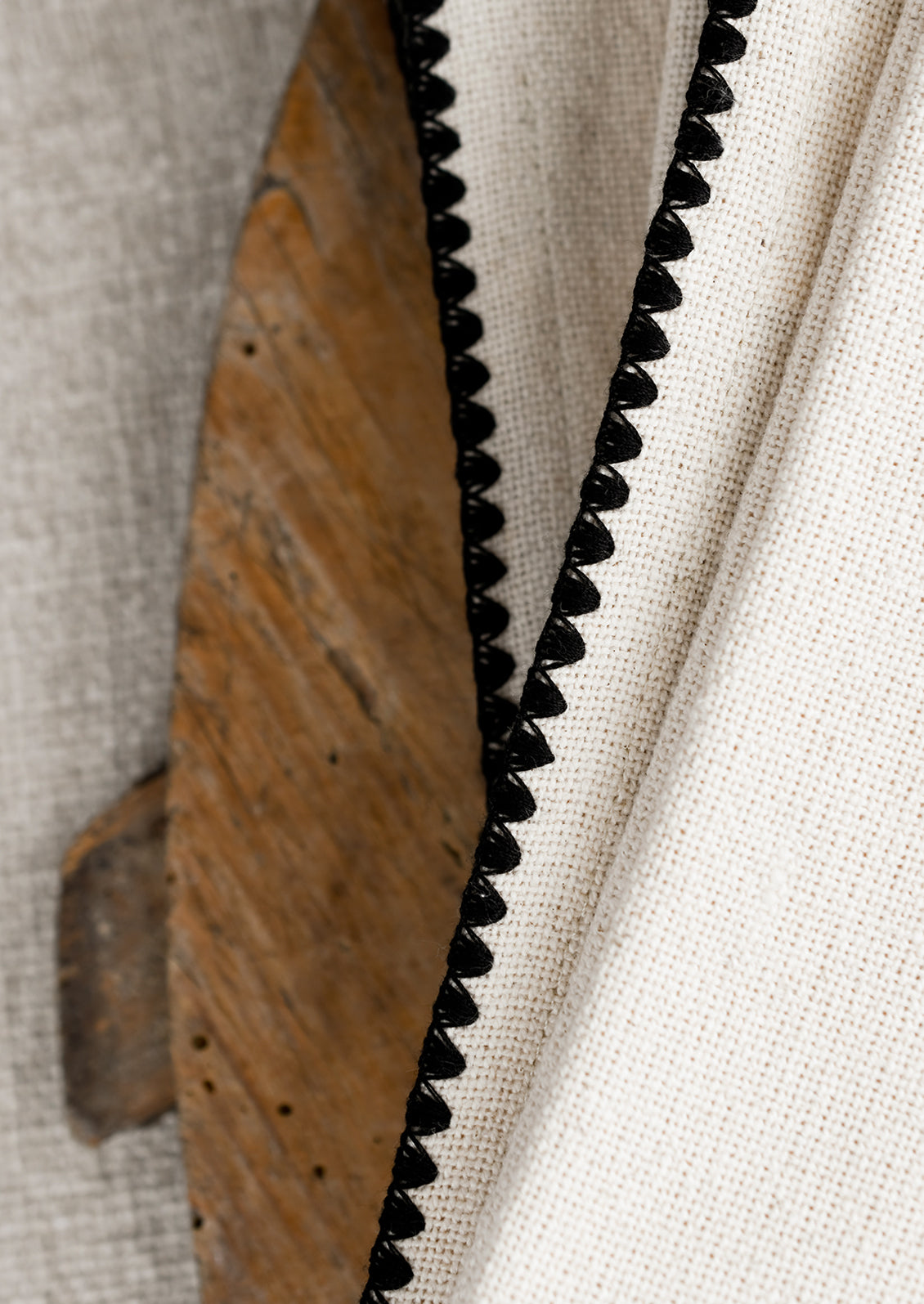 A stack of natural cotton dinner napkins with scalloped black stitching.