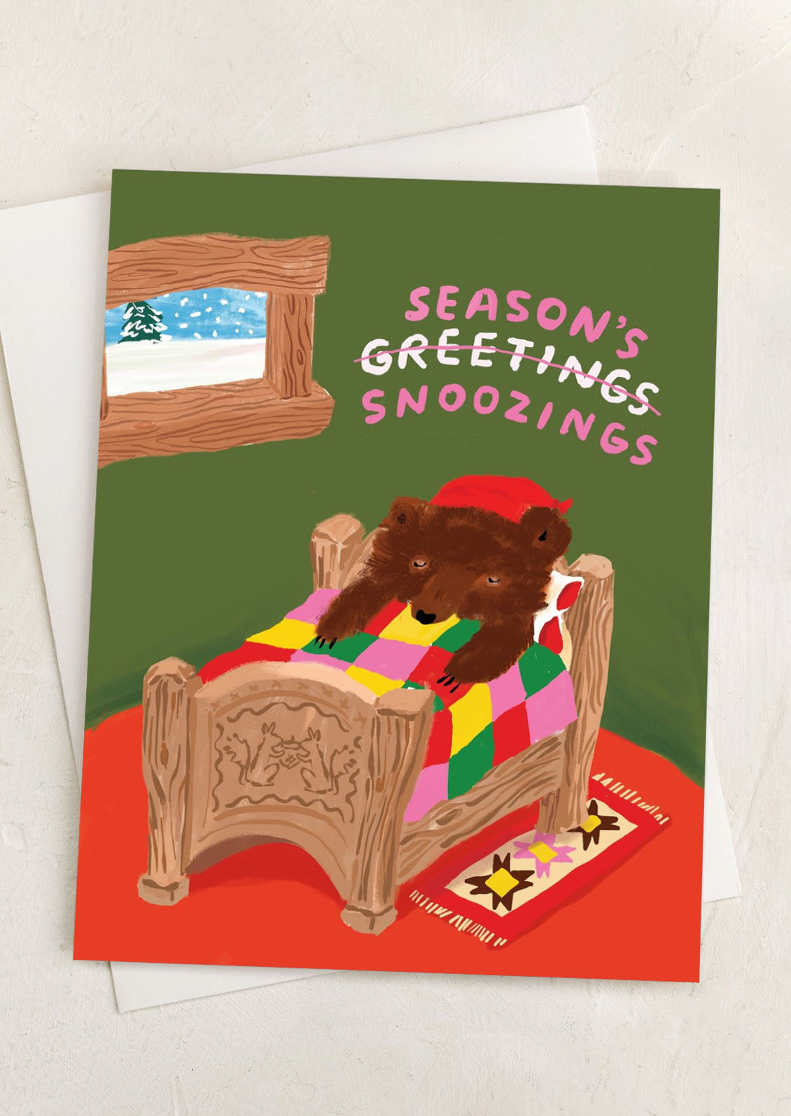 A greeting card with illustration of a bear in bed, text reads "Seasons Snoozings".