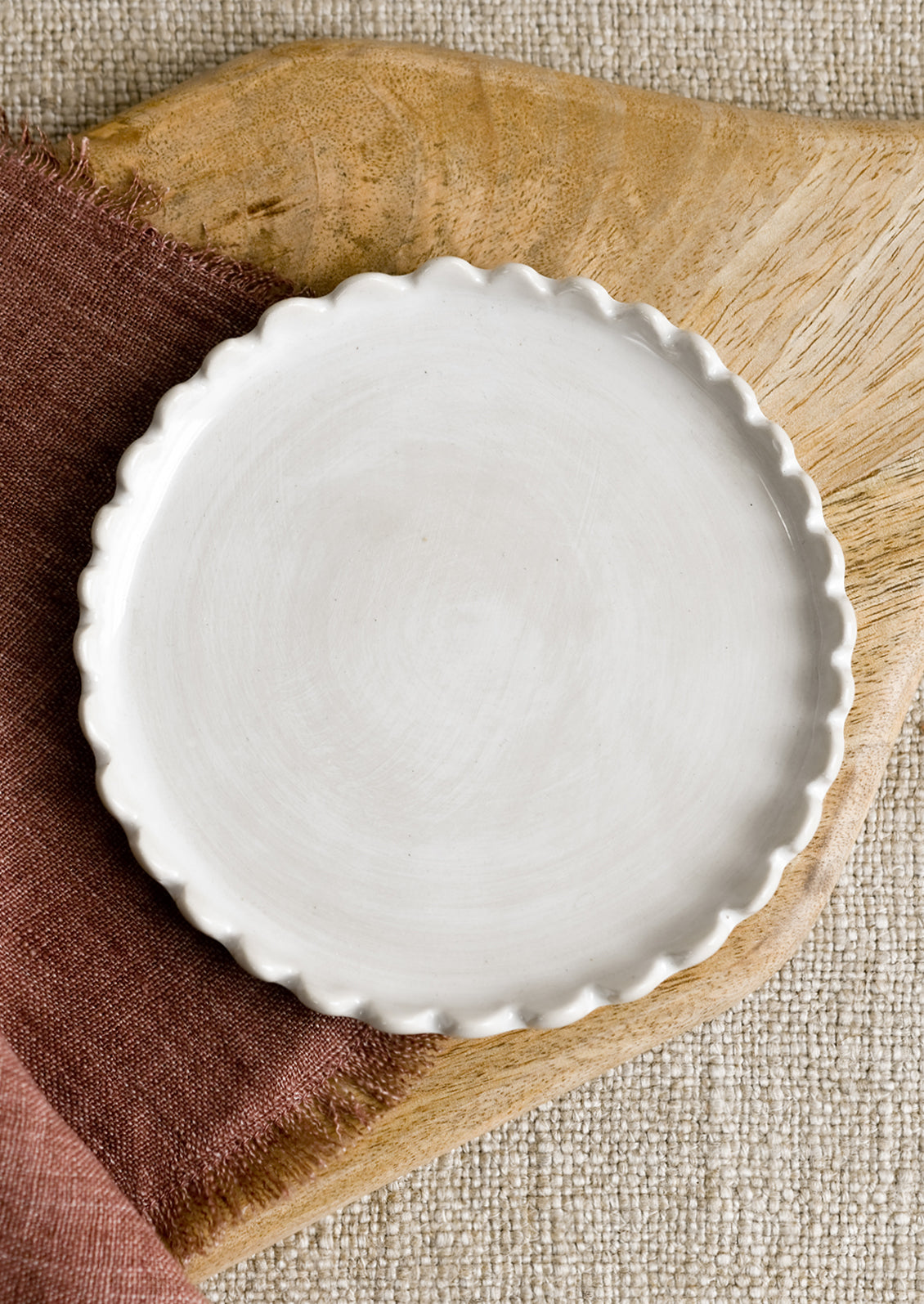 A round ceramic plate in white with scalloped edges.