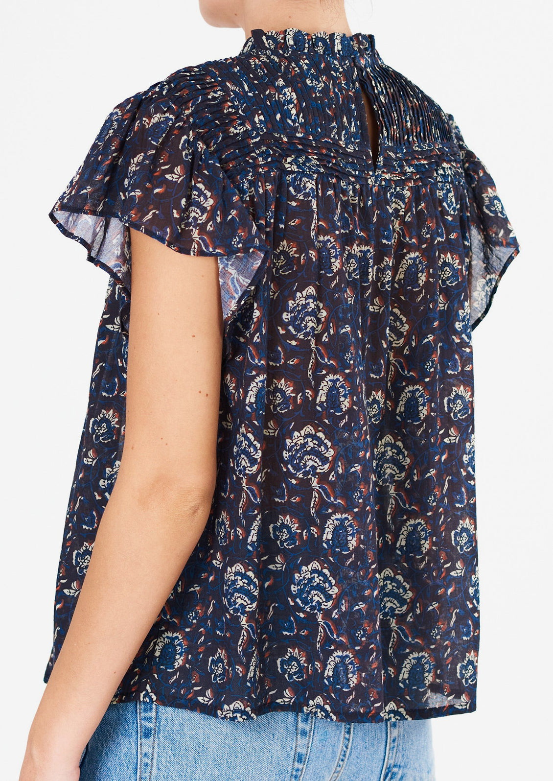 A woman wearing a blue, white and rust floral printed flutter sleeve top.