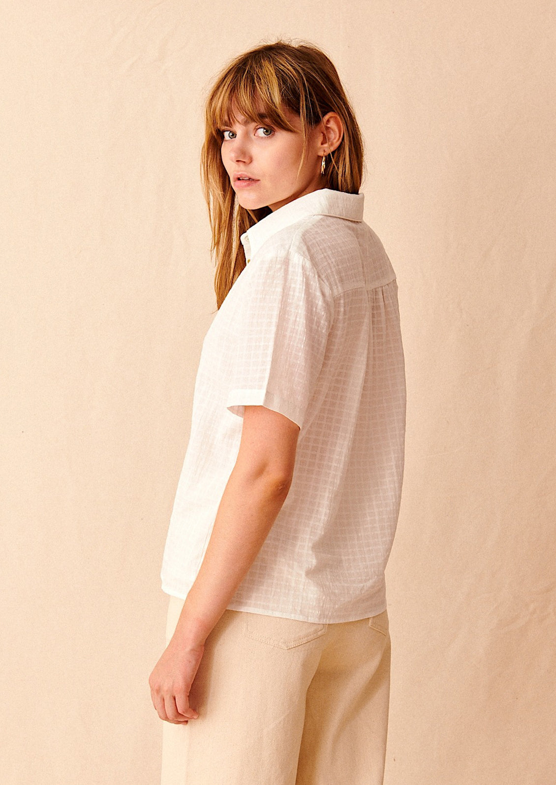 A woman wearing a short sleeve collared shirt with tonal grid texture.