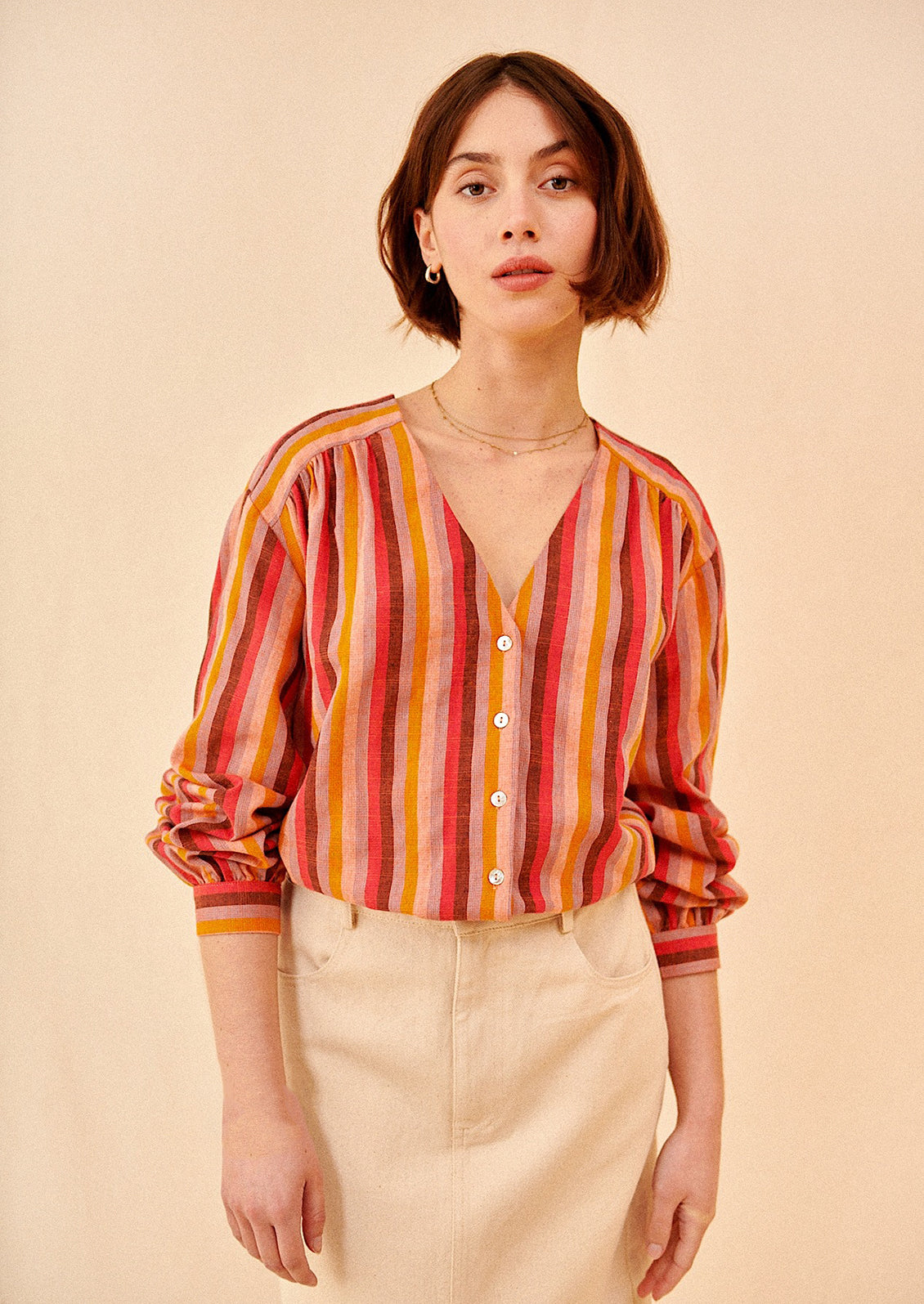 A woman wearing a v-neck, button front blouse in warm color stripe pattern.