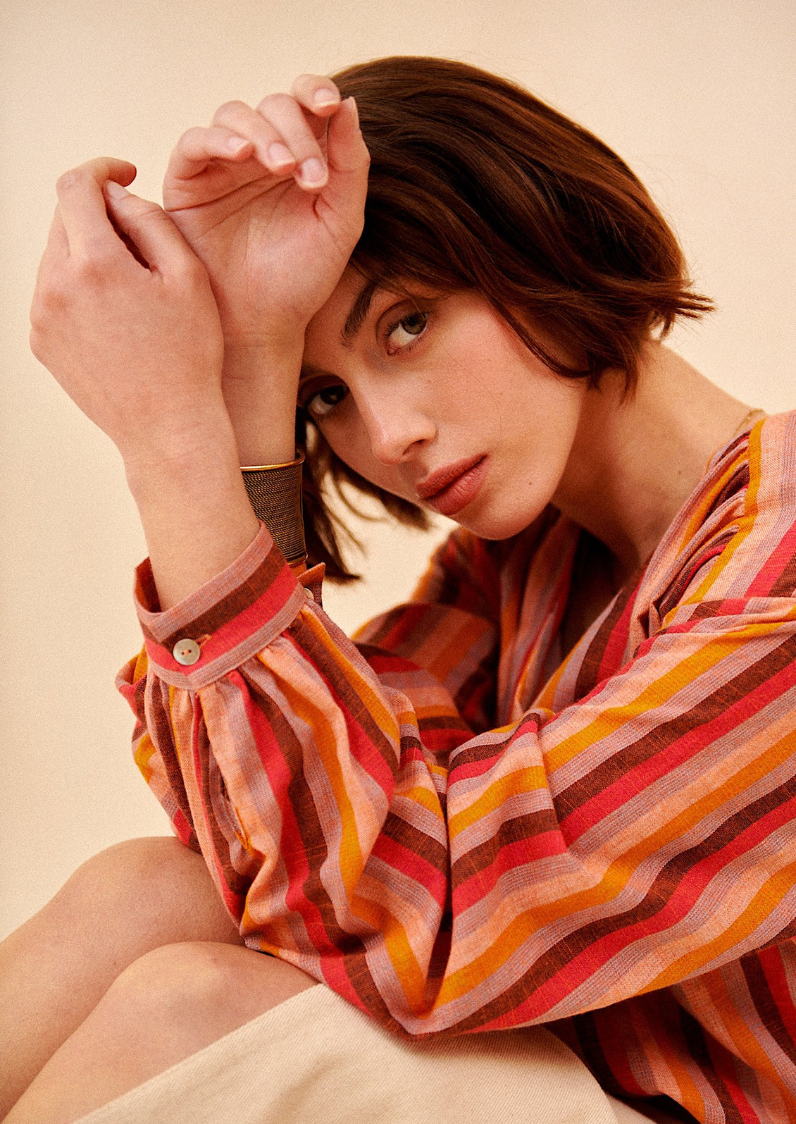 A woman wearing a v-neck, button front blouse in warm color stripe pattern.