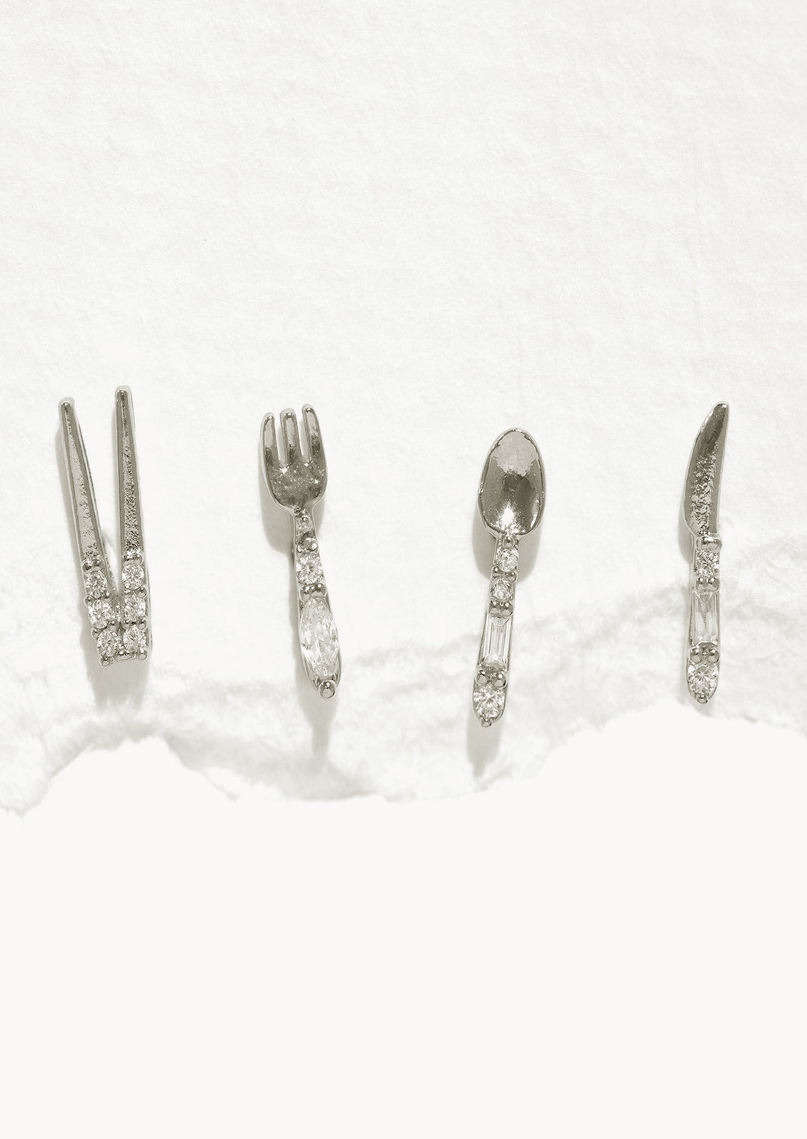 A set of four silver stud earrings in shape of chopsticks, fork, spoon, and knife.