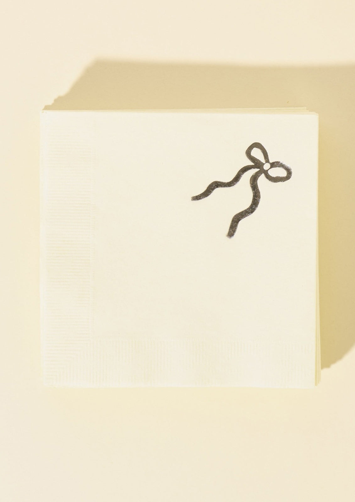 White paper napkins with silver foil bow graphic at corner.