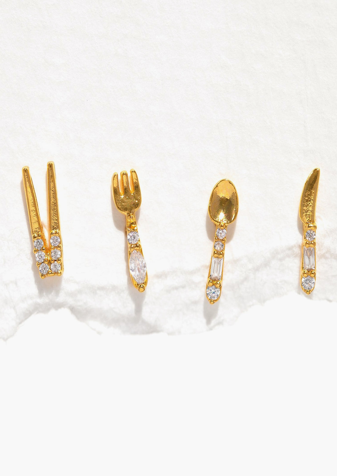 A set of four gold stud earrings in shape of chopsticks, fork, spoon, and knife.