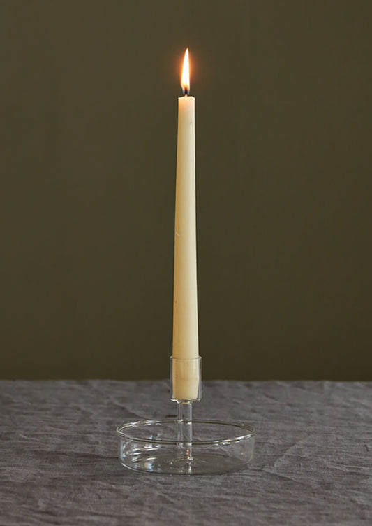 A clear glass candleholder with saucer-like base for catching drips.