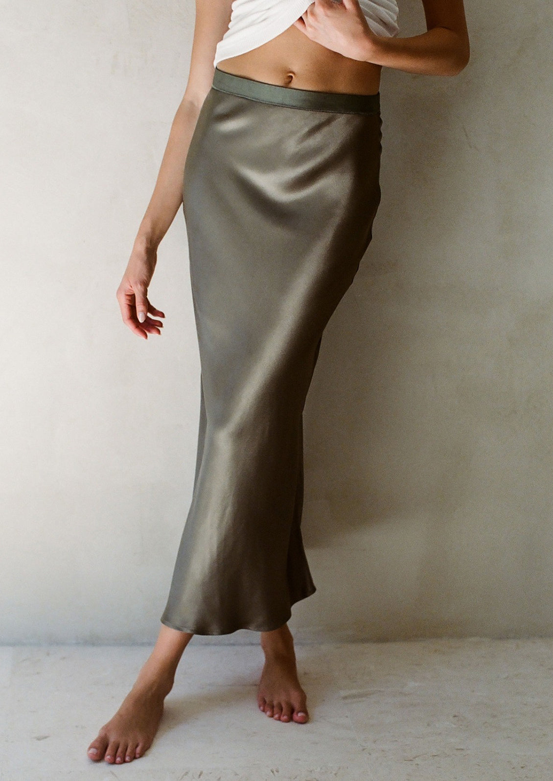 A woman wearing a form fitting skirt in olive green satin material.