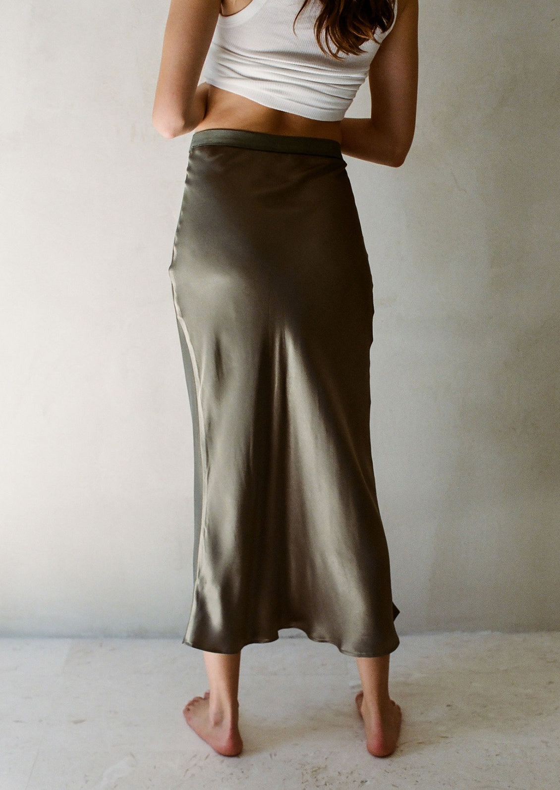 A woman wearing a form fitting skirt in olive green satin material.