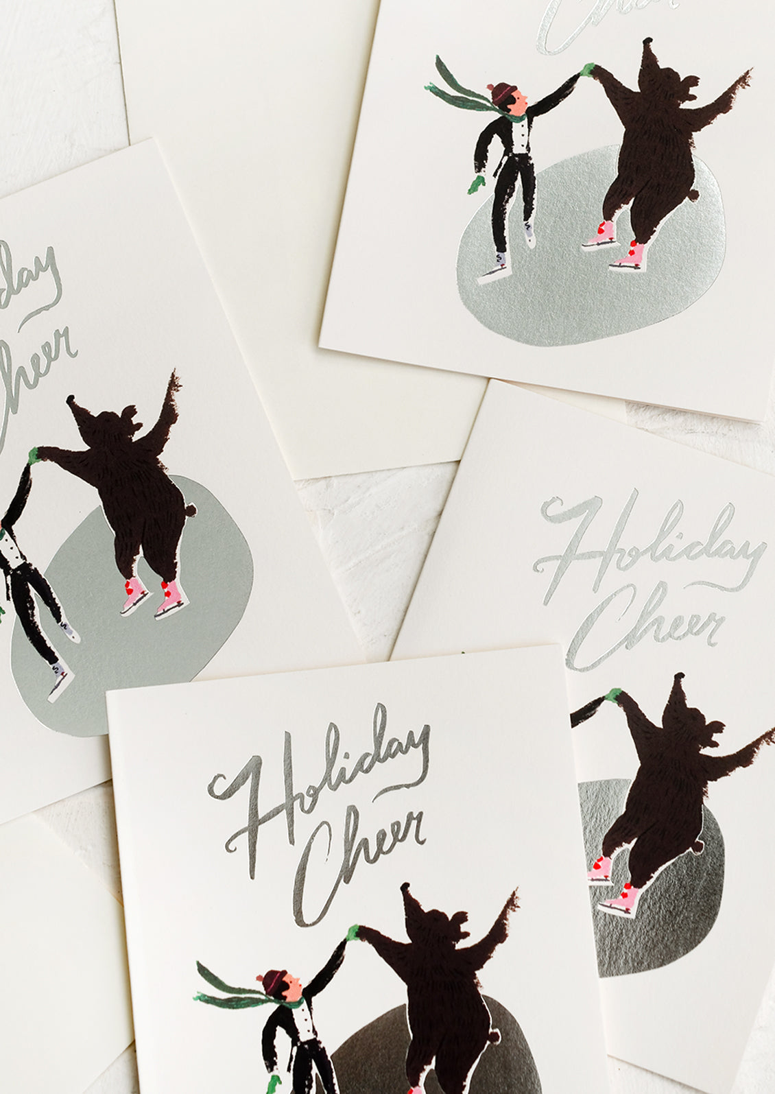 A set of cards depicting an ice skater and bear skating on silver pond, text reads "Holiday cheer".