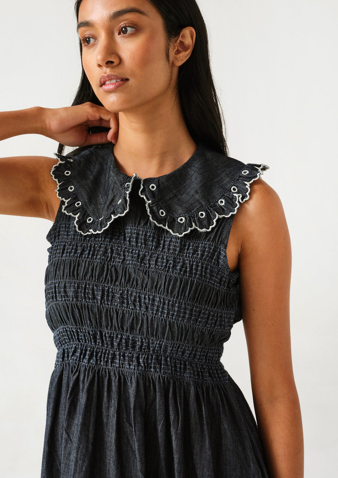 A woman wearing a denim dress with a smocked bodice and an embroidered collar with white stitching.