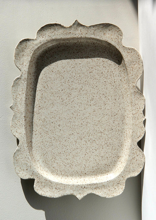 A rectangular shaped platter in speckled cream ceramic with wavy shape edge.