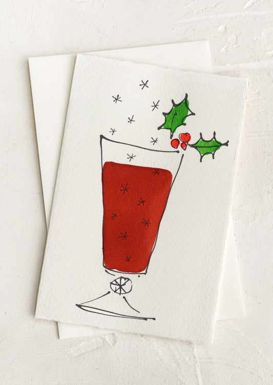 A greeting card with hand painted illustration of wine in glass, decorated with holly. There is no text.