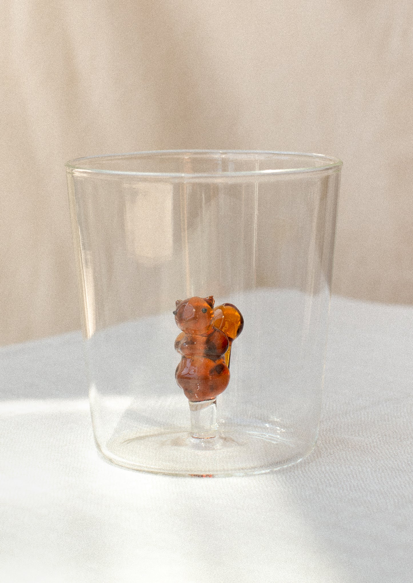 A clear glass cup with figurine of a squirrel at bottom.