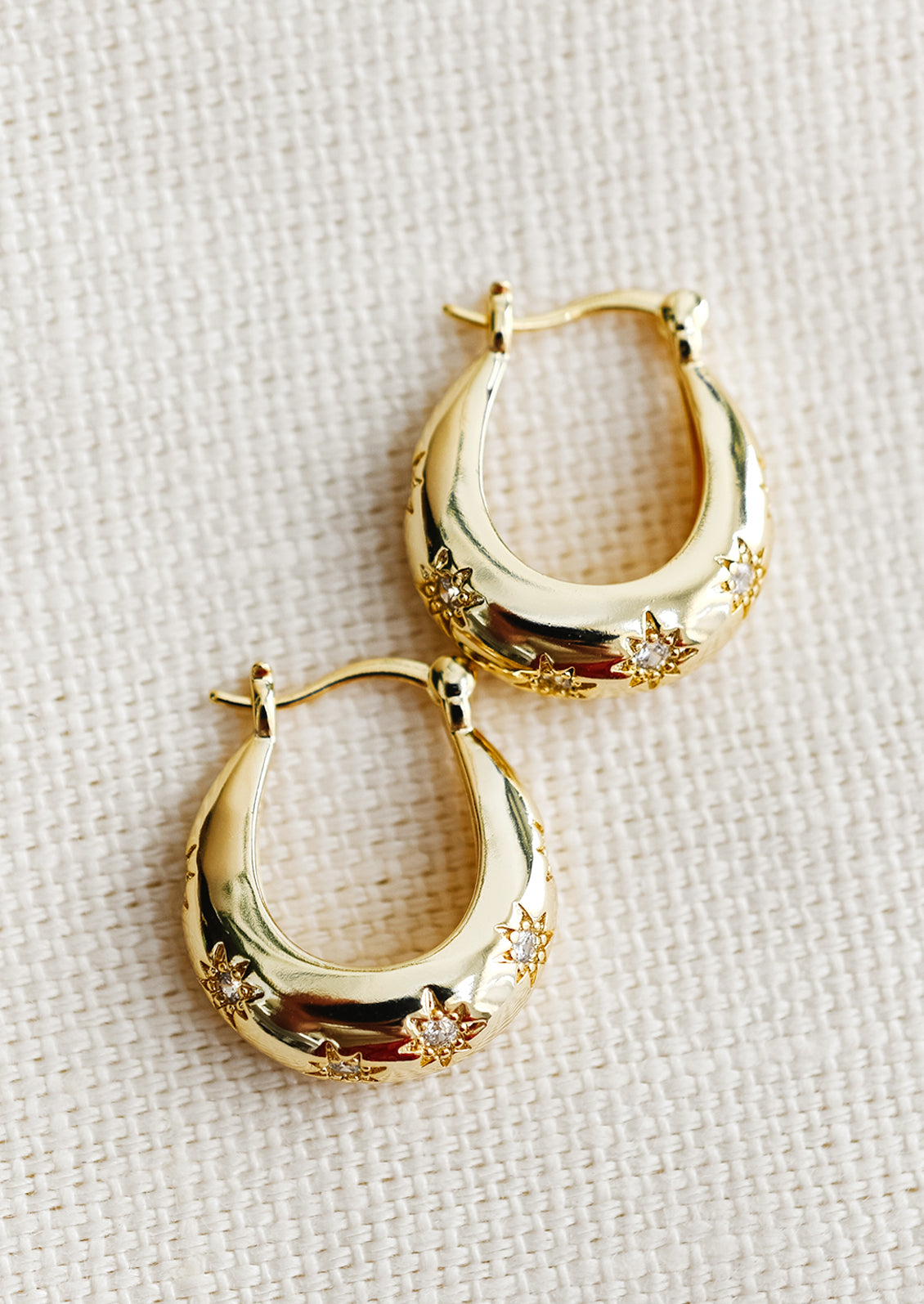 A pair of oblong oval hoops in gold with clear star shaped crystal detailing.