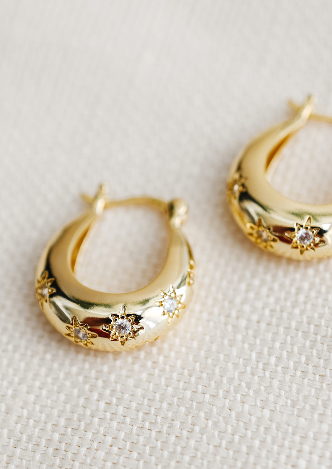 A pair of oblong oval hoops in gold with clear star shaped crystal detailing.