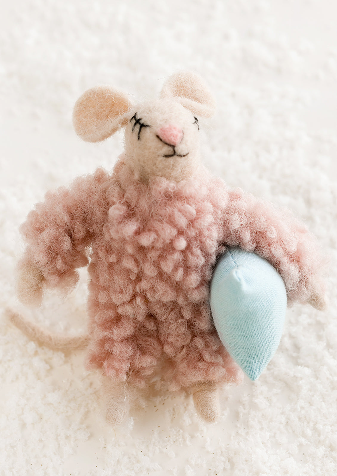 A felted mouse ornament in pink fuzzy pajamas, holding a blue pillow.