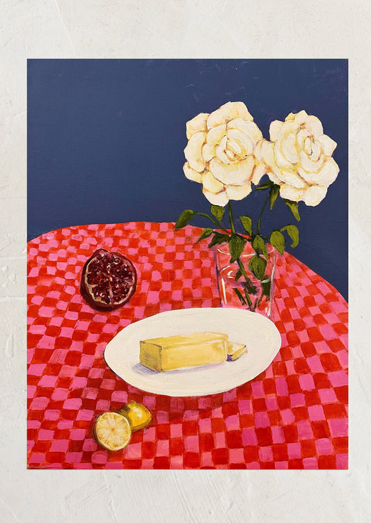 An art print of a still life painting depicting white roses, a pomegranate, and stick of butter on a checkered tablecloth.