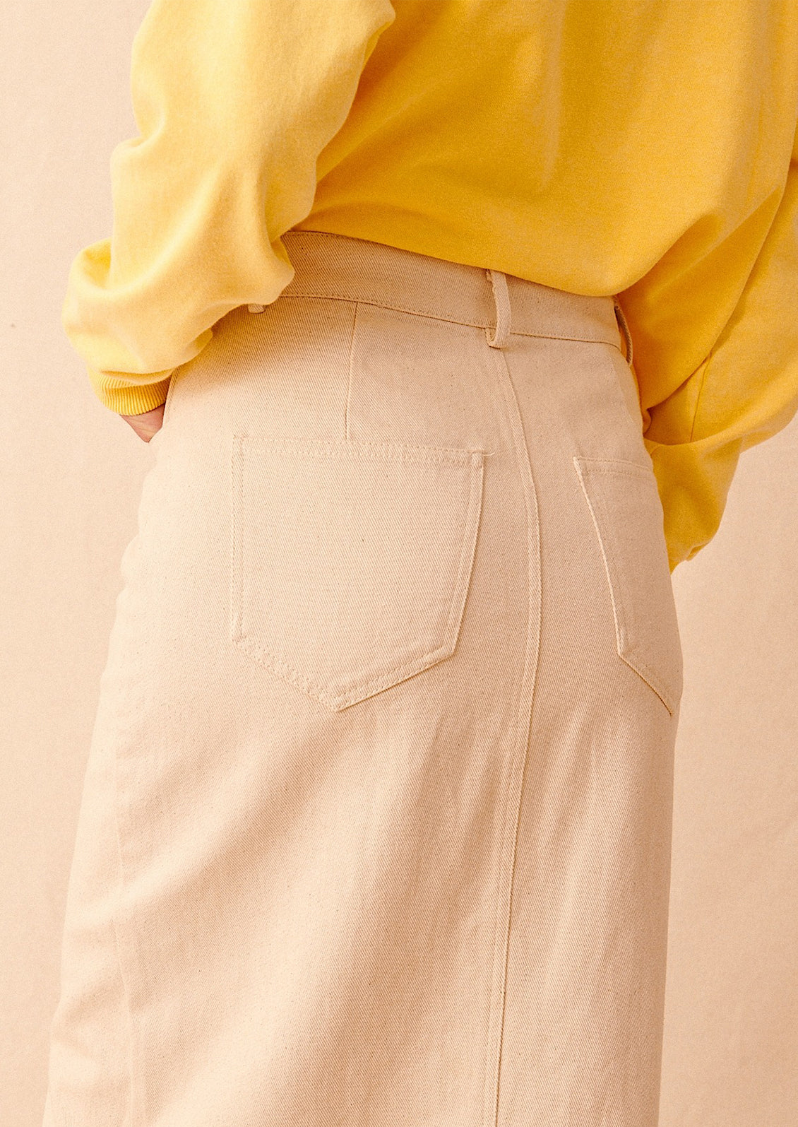 A person wearing a yellow sweatshirt tucked into an ecru denim skirt showing back pocket detail