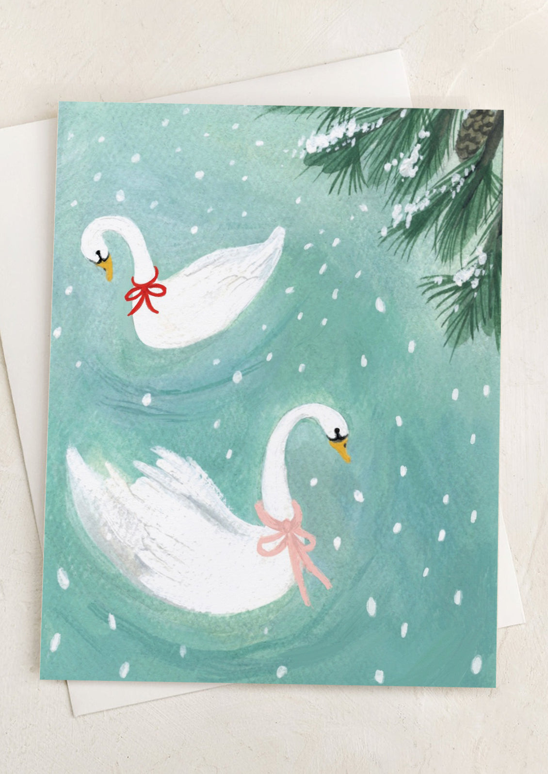 A greeting card with illustration of swans wearing ribbons, in snowy lake.