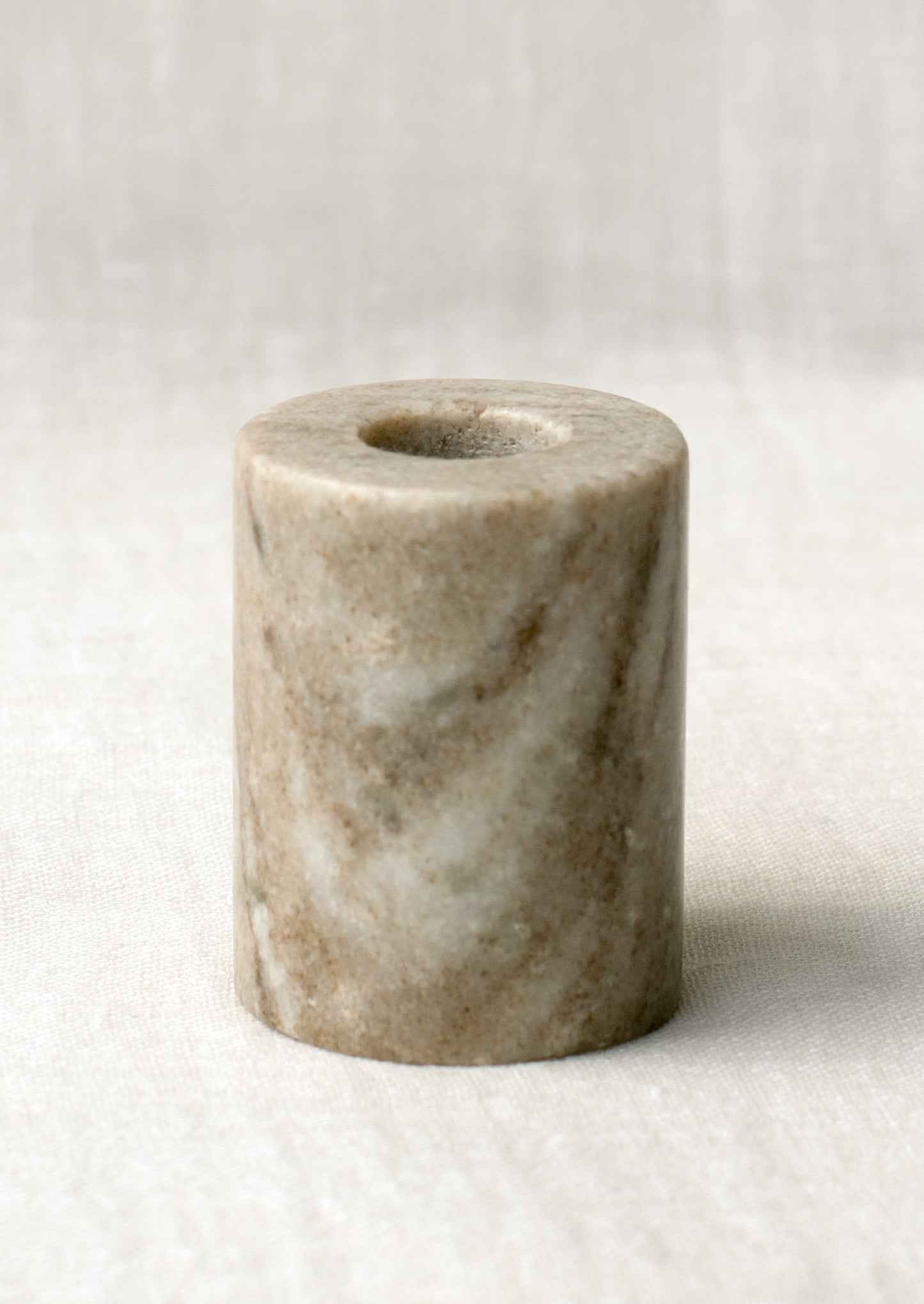 A cylindrical candleholder in solid taupe marble.