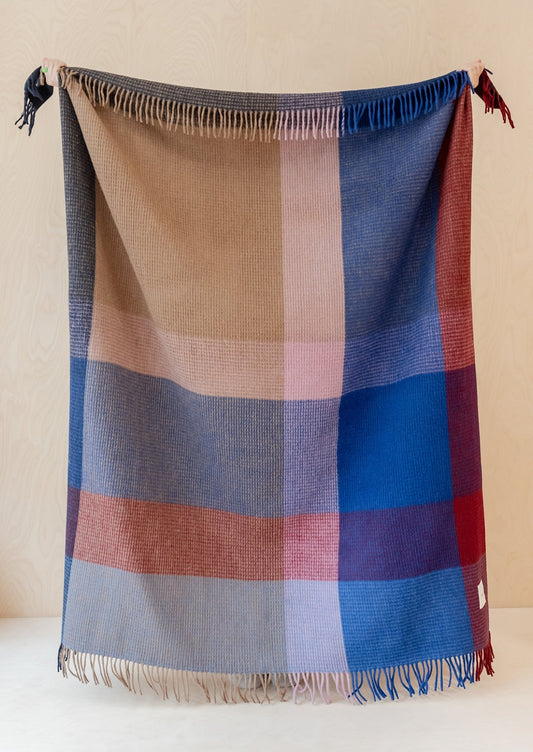 A colorblock grid print blanket with waffle texture in tones of red, cobalt blue and beige.