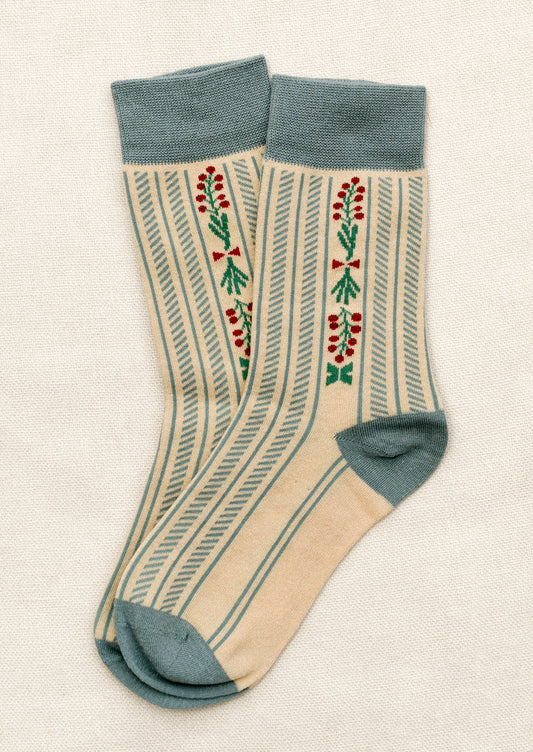 A pair of ivory socks with dusty blue vertical stripe and trim, red berry floral pattern throughout.