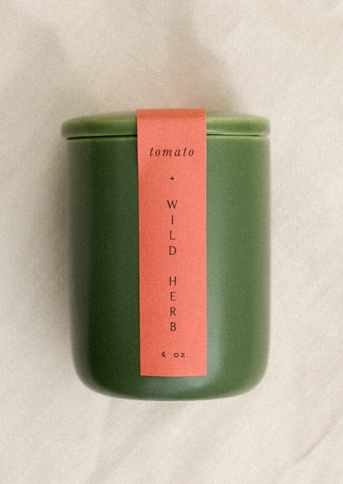 A small candle in lidded green ceramic jar in Tomato & Wild Herb scent.