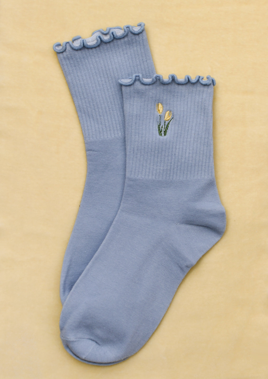 A pair of periwinkle blue socks with embroidered tulip motif in butter yellow.