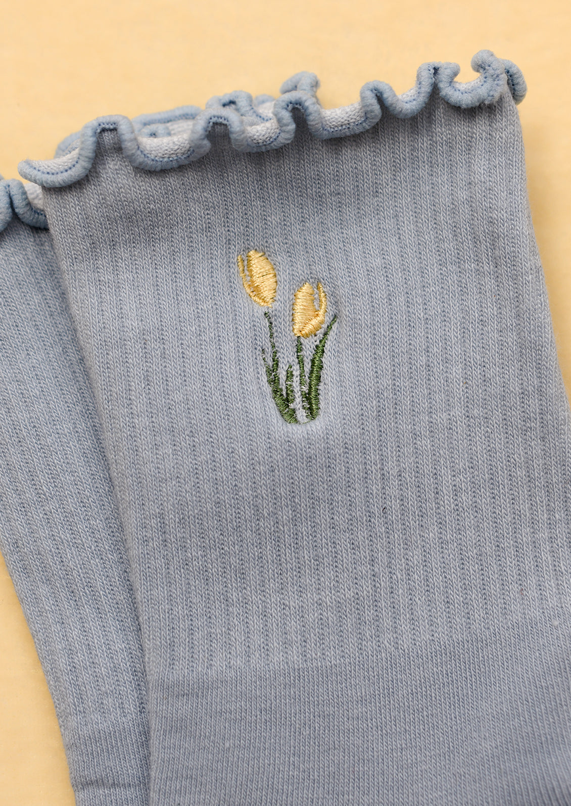 A pair of periwinkle blue socks with embroidered tulip motif in butter yellow.