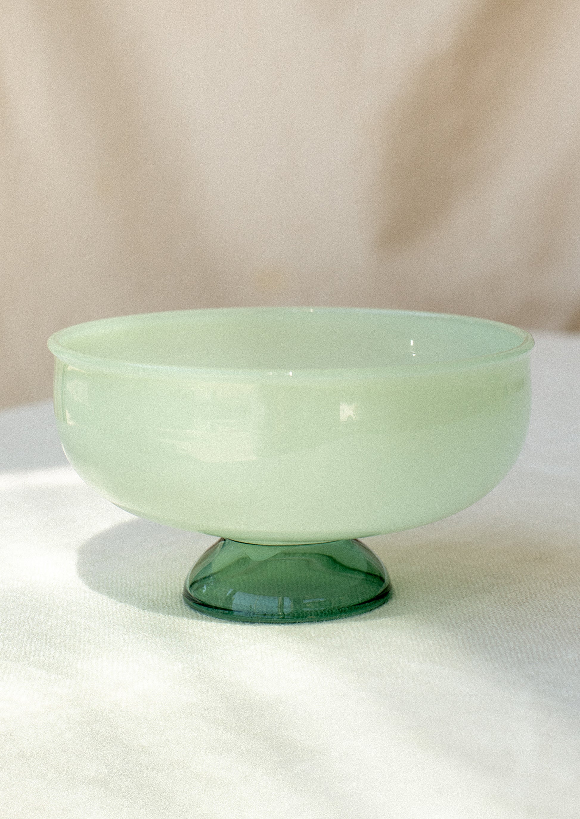 A shallow glass bowl with opaque mint top and clear emerald foot.