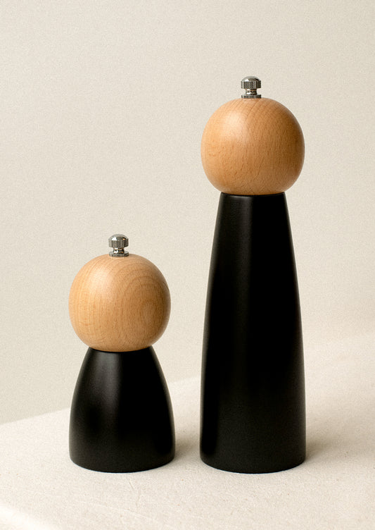 Tall and short pepper grinders with light round top and tapered black bottom.