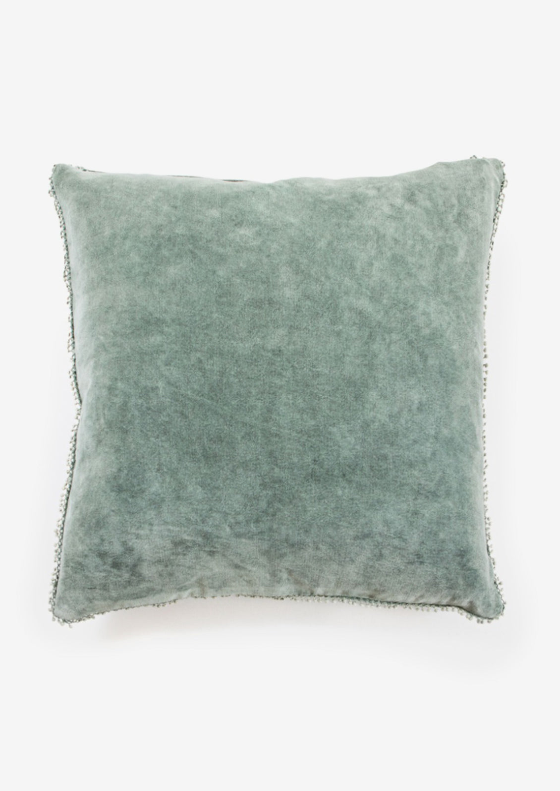 A velvet throw pillow with pom pom trim in juniper color.