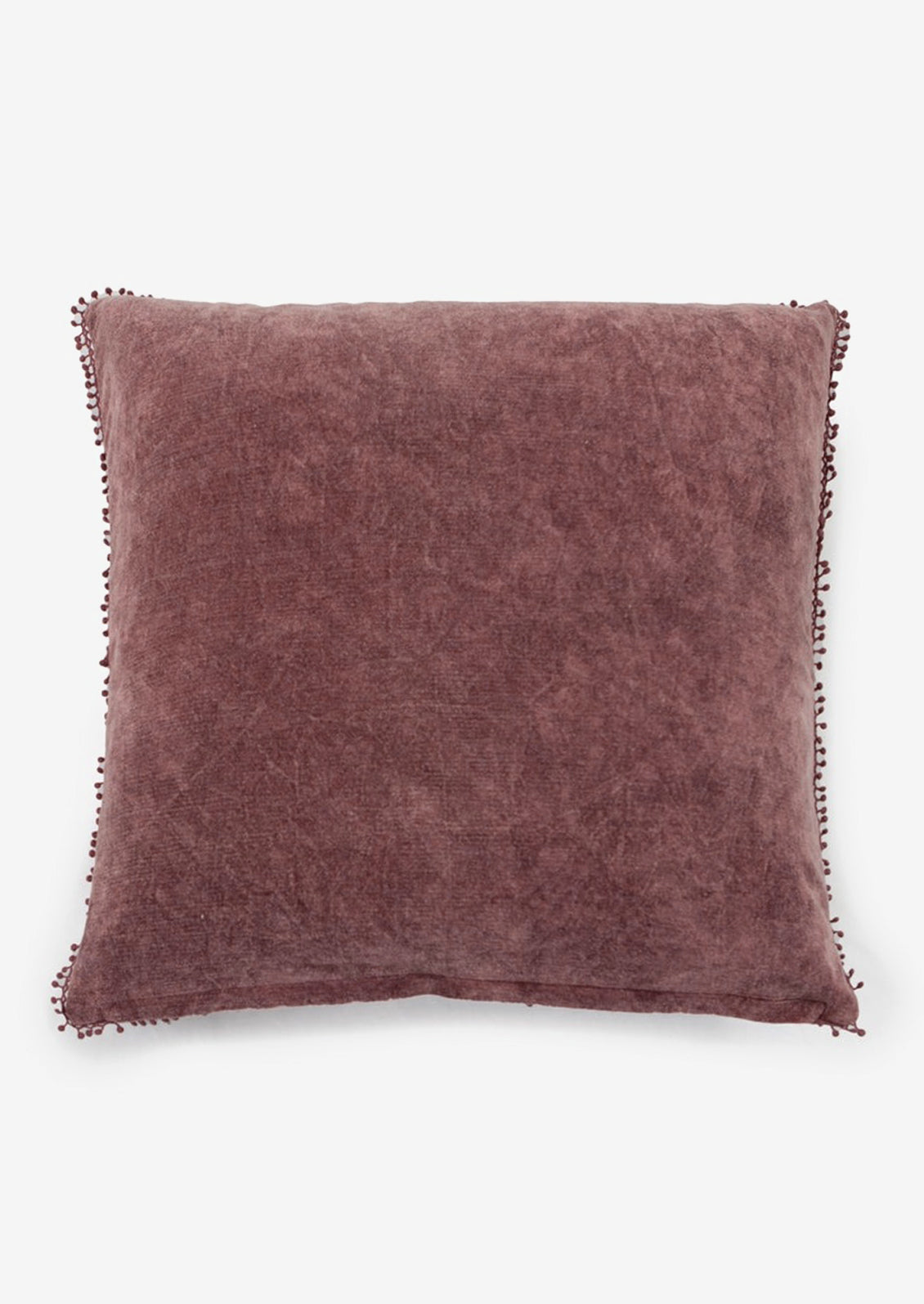 A velvet throw pillow with pom pom trim in plum color.