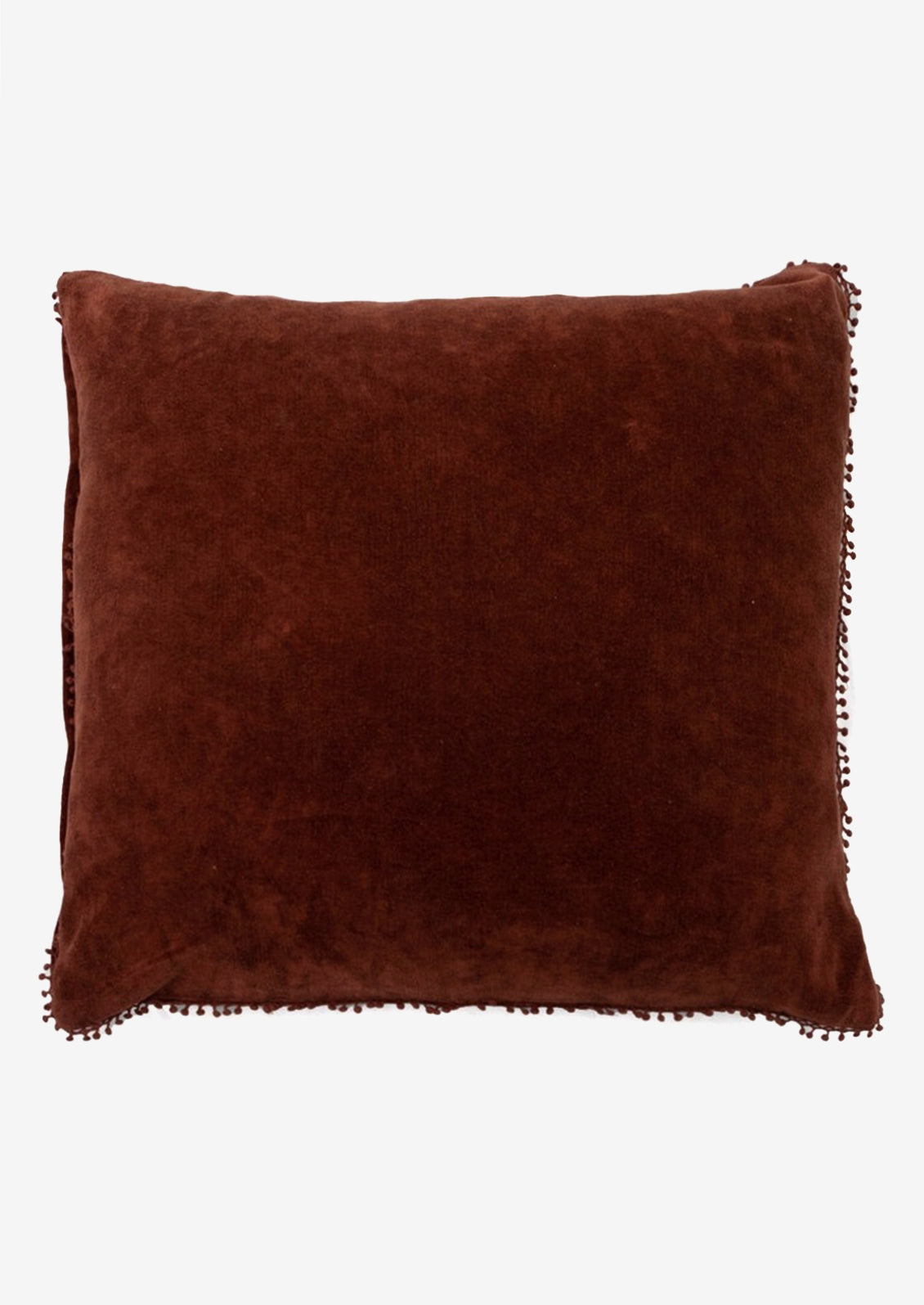 A velvet throw pillow with pom pom trim in rust color.