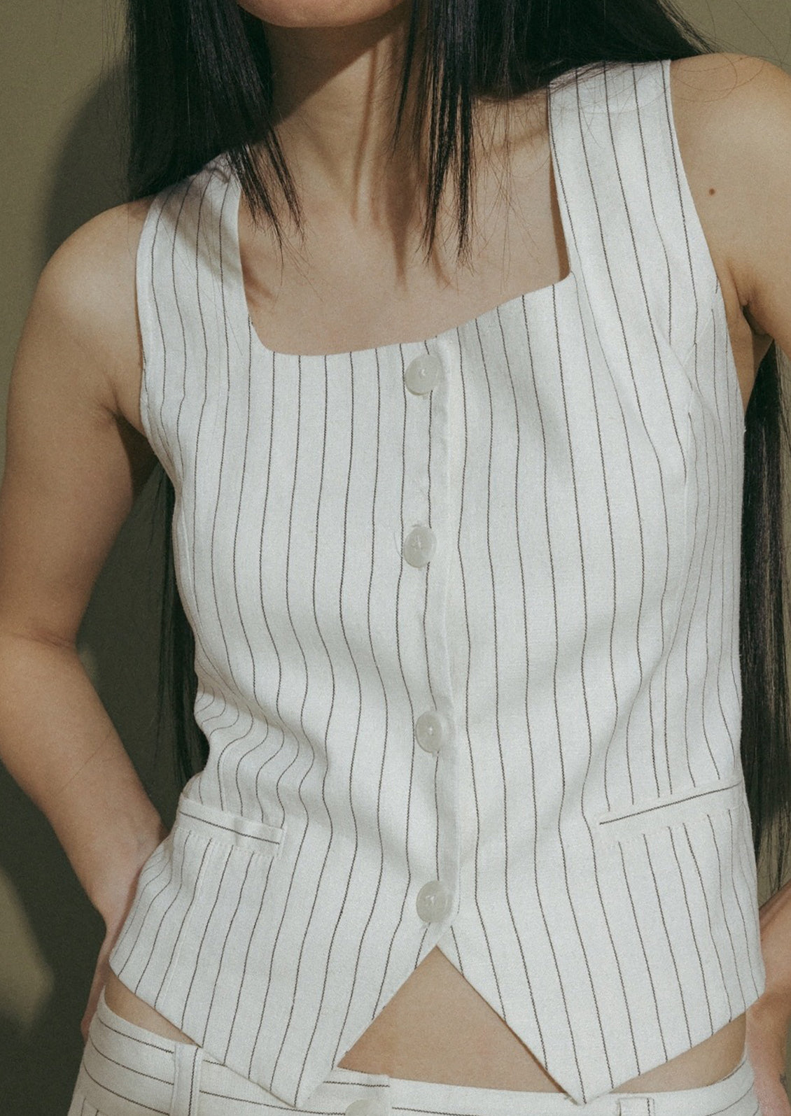 A woman wearing a white baseball style vest with black pinstripe.