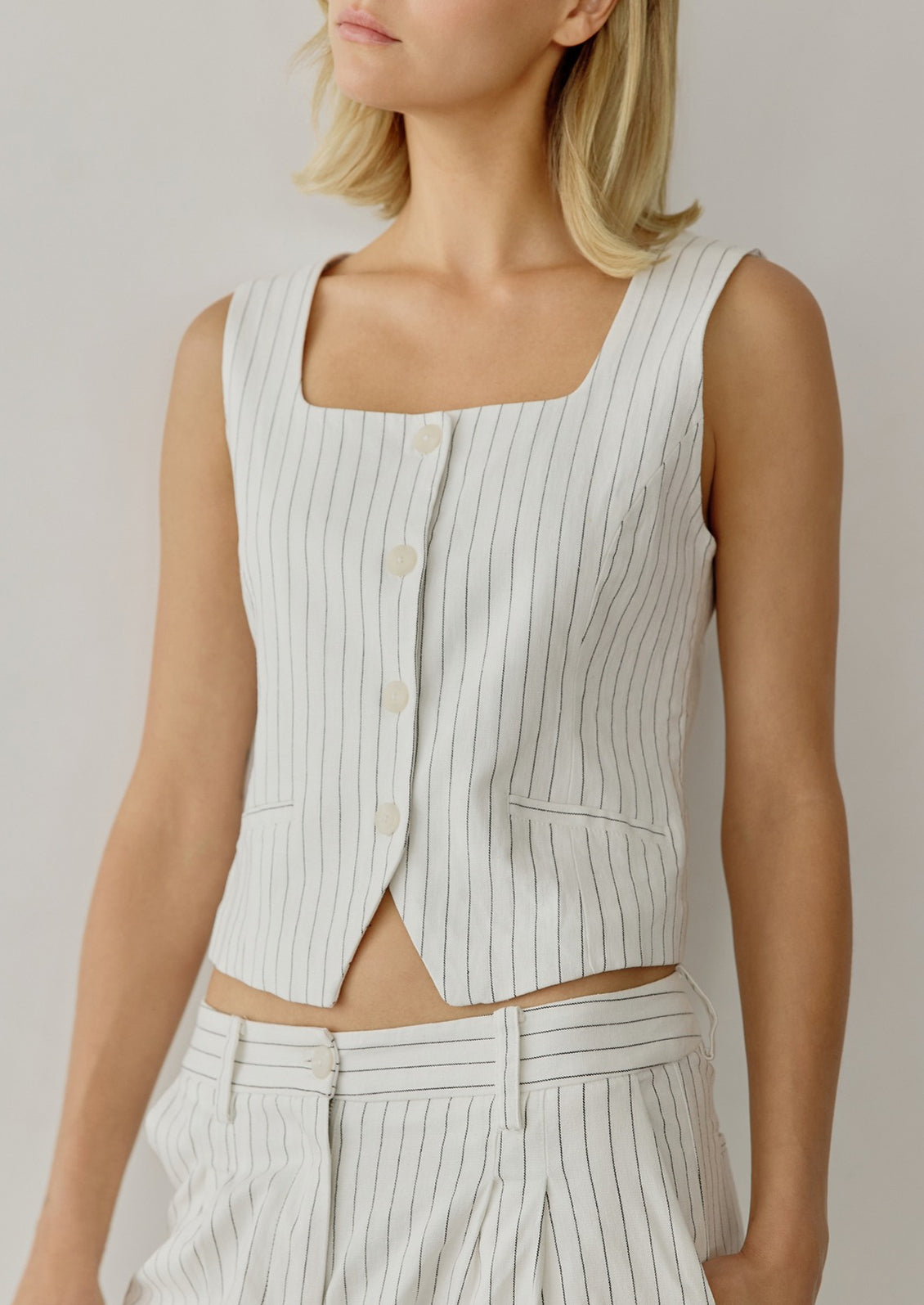 A woman wearing a white baseball style vest with black pinstripe.