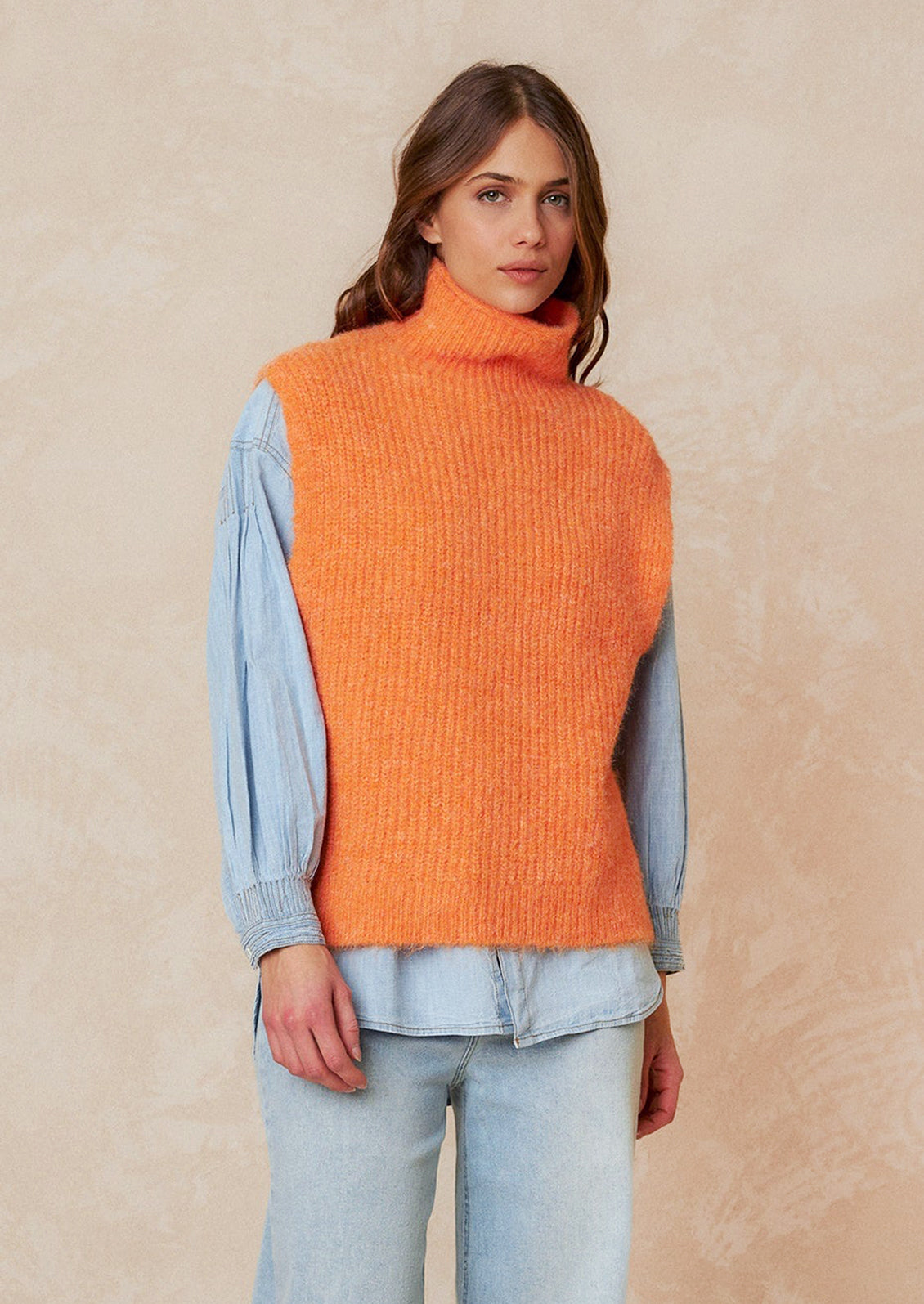 A woman wearing a sleeveless turtleneck sweater in orange.