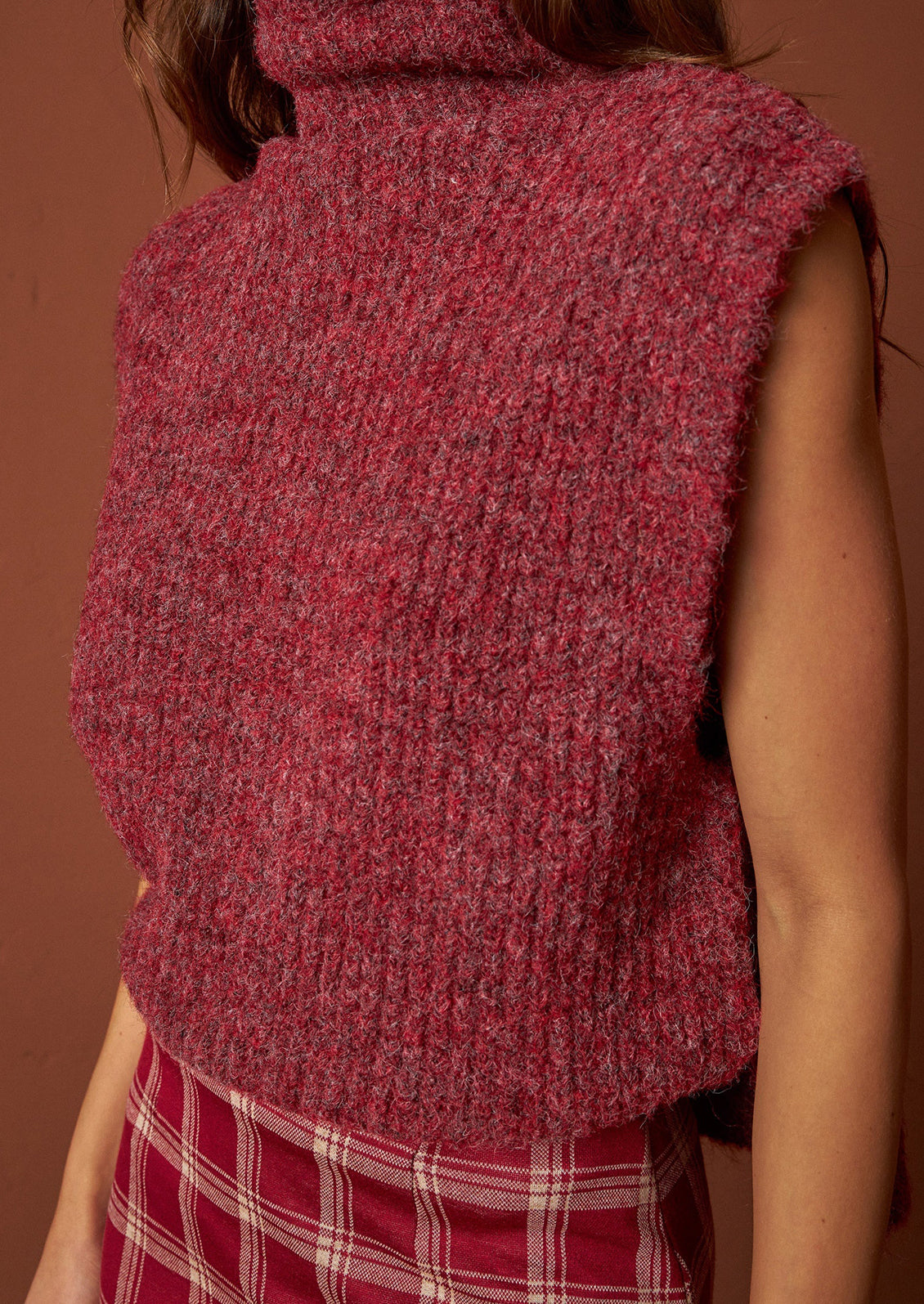 A woman wearing a sleeveless turtleneck sweater in wine red.