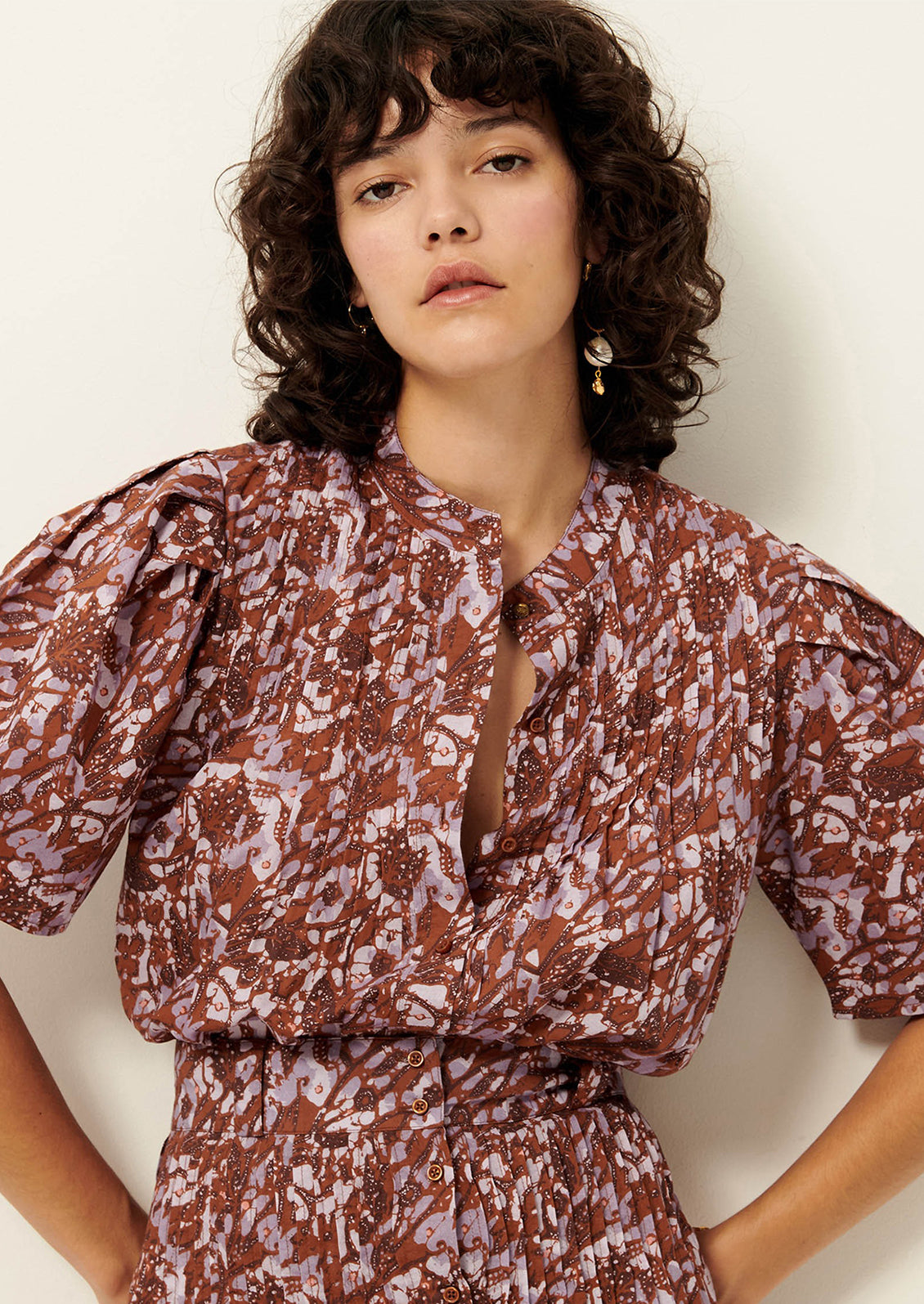 A woman wearing an abstract printed purple and rust colored button up top with short sleeves.