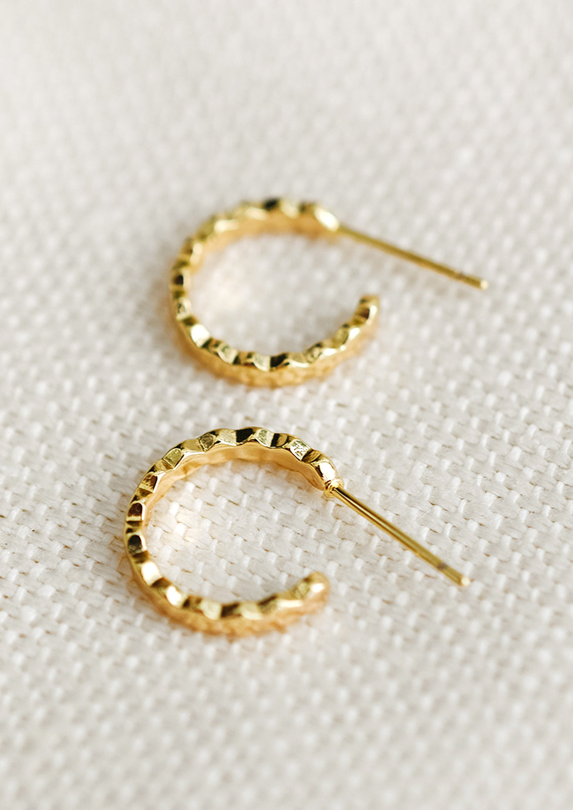 A pair of small gold hoop earrings with wavy shape.