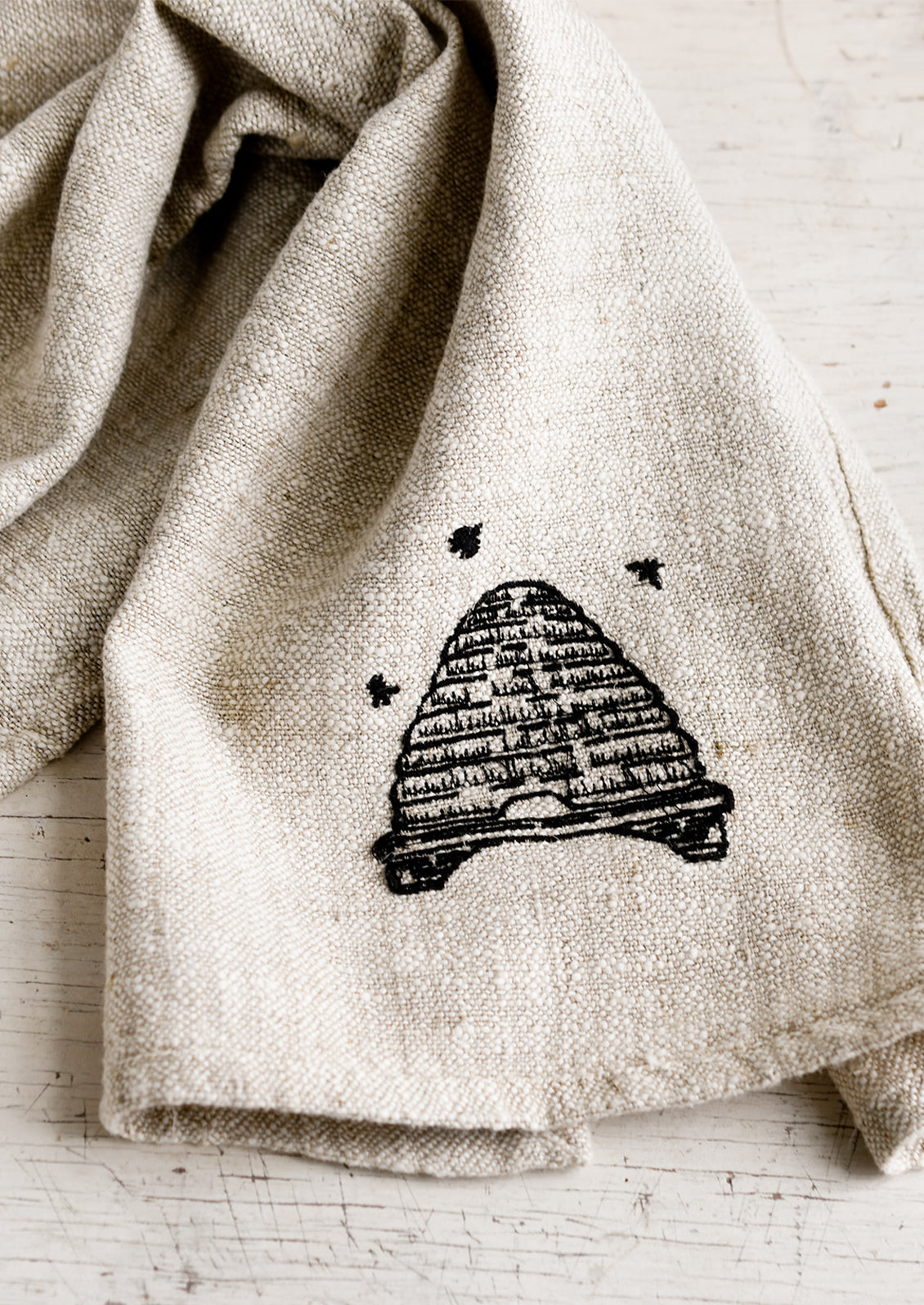 A natural linen tea towel embroidered with beehive in black stitching.