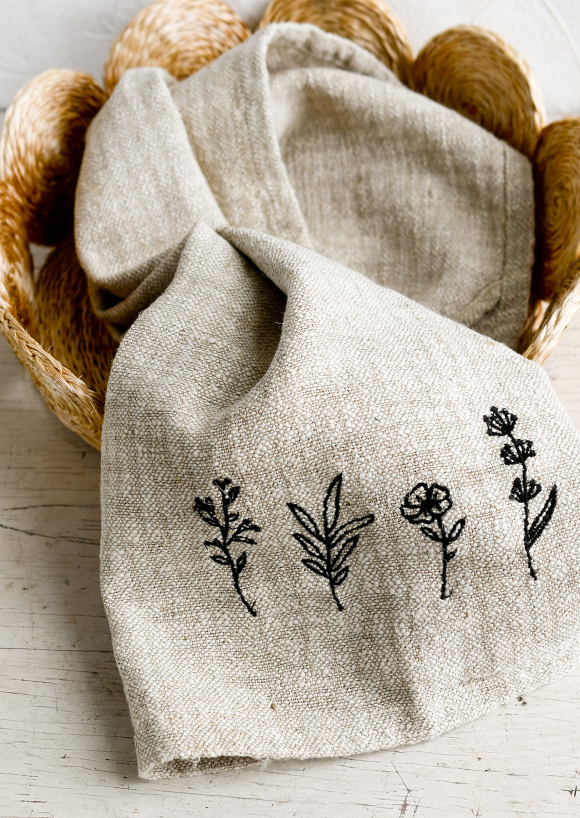 A natural linen tea towel embroidered with flowers in black stitching.