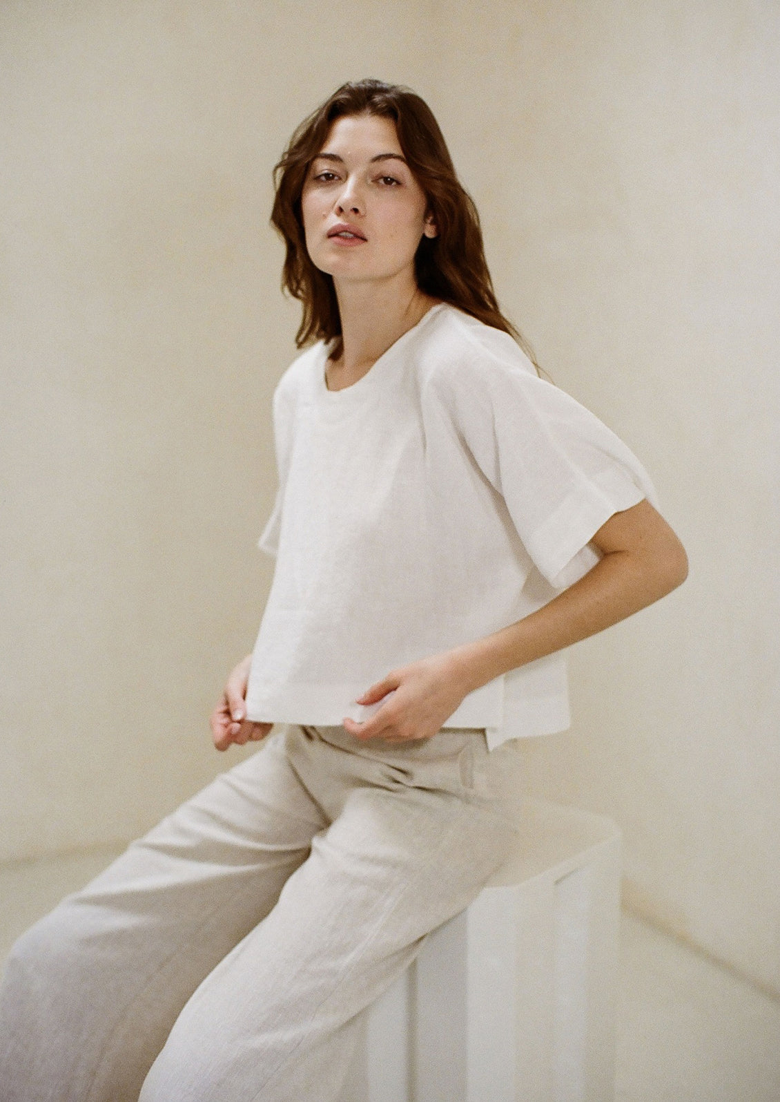 A woman wearing a white short sleeve linen top and light pants. 