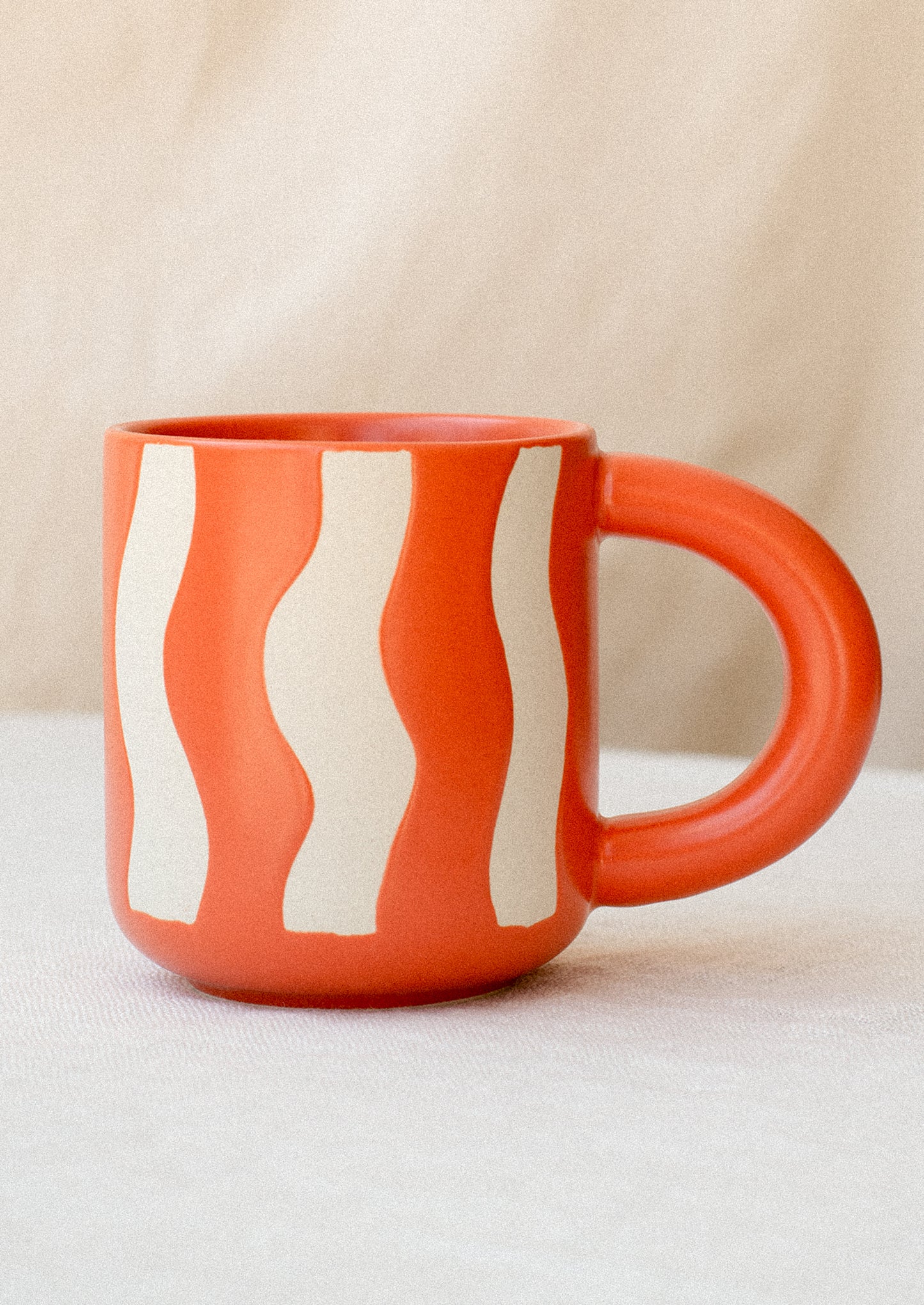 A ceramic mug in bright orange with wax relief wavy stripe pattern.