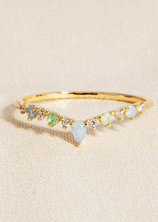 A gold ring in pointed wishbone like shape with green and pastel blue gemstones.