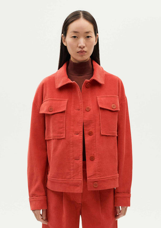 A woman wearing a shirt jacket style corduroy long sleeve jacket in red-orange hue.