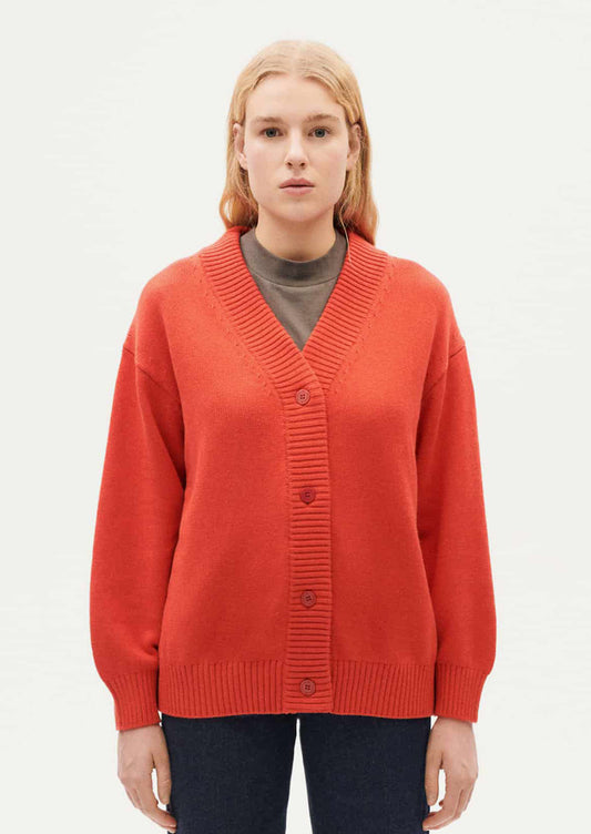 A woman wearing a button front, long sleeve cardigan sweater in red-orange huge.