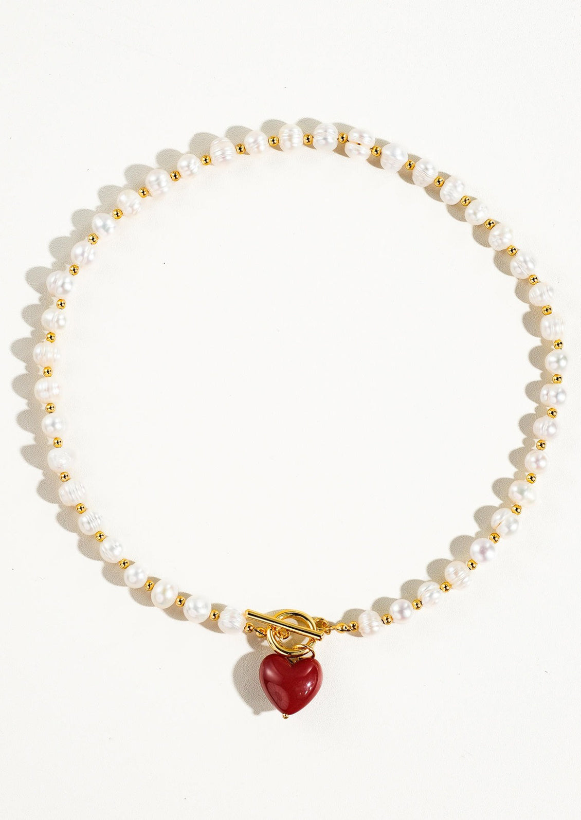 A necklace with alternating gold and pearl beads and red heart toggle clasp.