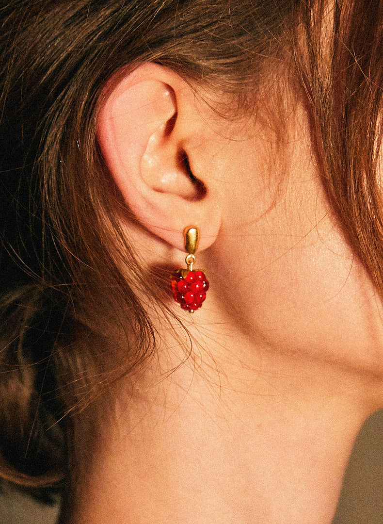 A person wearing a pair of glass earrings in shape of raspberries.